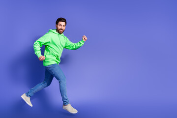 Full size photo of pretty young male running fast wear trendy green outfit isolated on purple color background