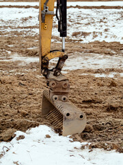 Close-up of an excavator arm digging dirt at a snowy construction site. Industrial work and equipment in winter conditions. © AFilipczuk