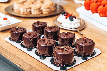 A decadent display of rich, glossy chocolate mini cakes topped with cocoa nibs and a touch of nuts. These indulgent desserts, perfect for a refined dessert table, feature a mirror glaze that enhances 