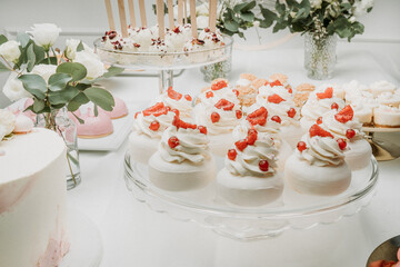 An elegant dessert table with meringue topped with cream, fresh raspberries, and red currants. The arrangement includes cake pops and delicate pastries, set against a soft white background with floral