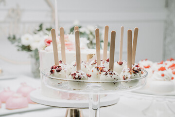 A stylish display of white chocolate cake pops with floral petal accents, presented on a glass stand. The delicate and artistic dessert setup exudes elegance, perfect for special occasions.