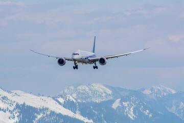 白い雲と青空、雪山のアルプス山脈を背景に飛行機が飛ぶ