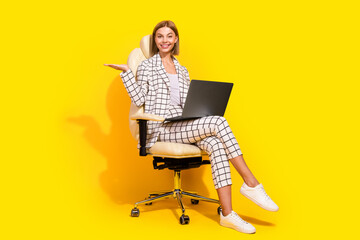 Charming young businesswoman in elegant suit working on laptop against vibrant yellow background