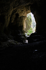 Silhouette of a big cave entrance from inside, water stream flowing into cave