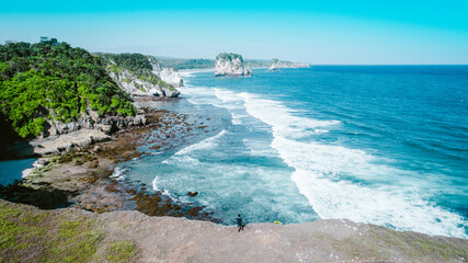 Aerial view of man standing on the rock with view waves crashing into coastal rocks