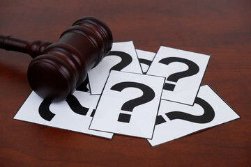 Legal FAQ concept. Wooden judge gavel and question marks on table.