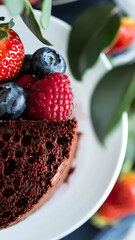 Decadent chocolate mousse cake topped with fresh strawberries, blueberries, and raspberries, garnished with green leaves, perfect for dessert lovers and special occasions.