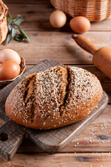 Rustic grain bread with oats, flax seeds, sunflower seeds and sesame seeds on a cutting board with a rolling pin on the background