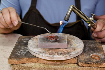 jeweler uses a blowtorch to solder a metal ring on a heat-resistant surface. This image captures craftsmanship and precision in jewelry-making. Ideal for topics on artisanship, jewelry, and metalwork.