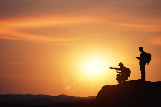 Planning and direction setting ideas. business concept with silhouettes of two businessmen planning trip on mountain with sunset background.