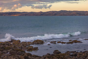 Waves crashing into coastal rocks at sunset. Dramatic sea coast background. Raglan, New Zealand