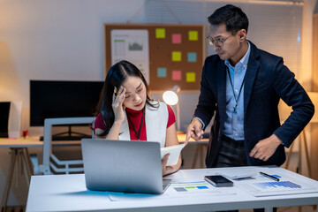 Asian businessman blaming stressed businesswoman working overtime in office at night