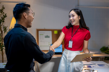 Asian business partners shaking hands during meeting in office at night