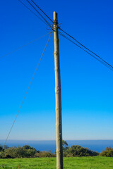 Obraz premium Poste de electricidad en ladera verde junto al mar