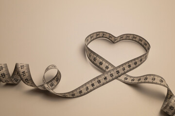  White centimeter tape in the shape of a heart with black numbers on a solid light colored background.