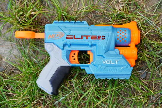 Plastic Nerf toy with orange and blue handles, resting on a patch of grass