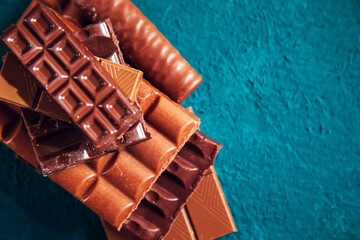 Broken pieces of dark and milk chocolate  on turquoise background.