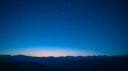 Fototapeta premium A vast night sky with a few stars and a faint sunrise over a mountain range.