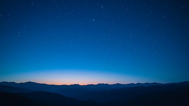 A vast night sky with a few stars and a faint sunrise over a mountain range.