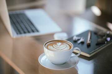 A cup of coffee is placed near a laptop on a table with space for copying documents, suggesting a break from work or a relaxing time at a cafe.