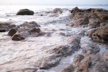 Close-up of rugged coastal rocks surrounded by soft waves under natural evening light. A calming scene showcasing the textured beauty of seaside landscapes.