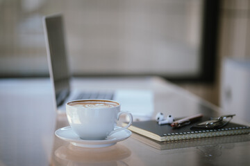 A cup of coffee is placed near a laptop on a table with space for copying documents, suggesting a break from work or a relaxing time at a cafe.