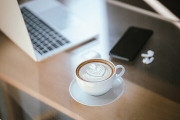 A cup of coffee is placed near a laptop on a table with space for copying documents, suggesting a break from work or a relaxing time at a cafe.