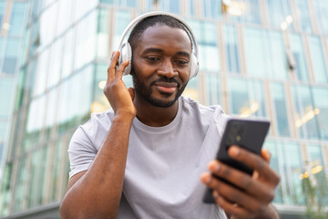 Music song concept. Good start day. Happy African American man listening modern hit on street in city. Person guy wearing headphones enjoy listening favorite music on phone. People lifestyle joy