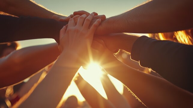 Diverse group of people putting their hands together in a circle, symbolizing unity and teamwork. The sun shines brightly in the background.