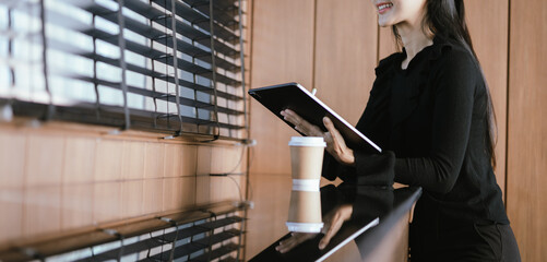 A beautiful young Asian woman in casual clothes sits at a table in a coffee shop with her digital...