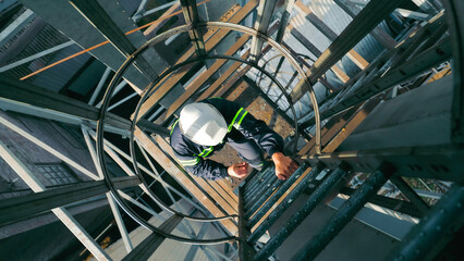 Worker Climbing Industrial Ladder with Safety Gear. Top view of a worker in a hard hat and...