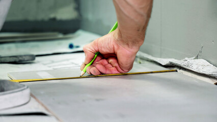 Close-up of Tiler Marking Floor Tile. A close-up of a workers hand marking a floor tile with a pencil, preparing for cutting and installation during tiling work.