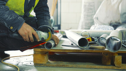 Worker cutting metal pipe with angle grinder in workshop. A worker uses an angle grinder to cut through metal pipes, creating a shower of sparks.