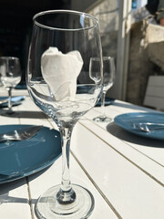 A close-up of a clear wine glass with a white napkin inside, placed on a white table set for an outdoor meal. 