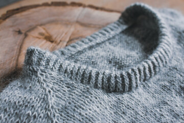 Gray cardigan sweater on wooden background, close up. Warm winter clothing. Rib sweater neck. Grey knitted sweater. Knitting pattern background. Cozy handmade clothes. Craft product close up