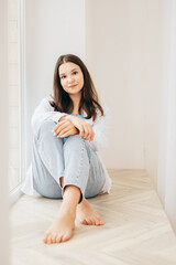 Naklejka premium A woman in a white shirt and jeans showing a stylish and understated look. The light background and natural pose give the shot a modern feel.