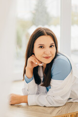 Obraz premium girl lying on her stomach on the windowsill, pensive look, slight smile in a white shirt and light jeans