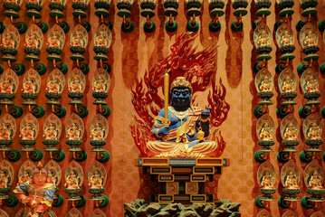 Medium shot of blue Acala Vidyaraja deity statue surrounded by a wall of smaller intricate god...