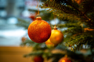 A close up of a glittery orange bauble on a festive tree, with selective focus