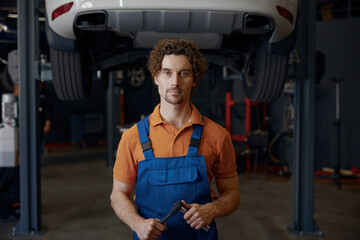 Man car mechanic looking at bottom of lifted automobile at repair station