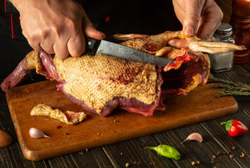 A chef expertly carves a whole duck, showcasing culinary skills on a wooden board, surrounded by fresh herbs and colorful spices, evoking a warm kitchen atmosphere