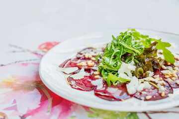 Close-up vibrant plate of beetroot carpaccio adorned with arugula, pine nuts, and Parmesan shavings, finished with a delicate dressing