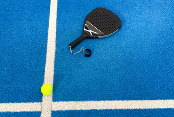 Black professional paddle tennis racket and ball with natural lighting on blue background....