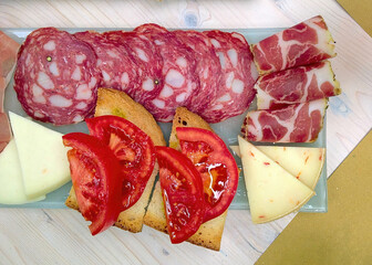 Italian appetizer platter featuring salami, coppa, cheese, tomato, and bread