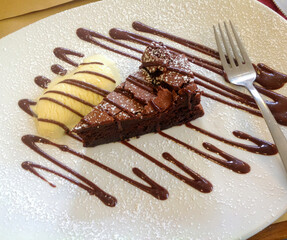 Chocolate cake slice with vanilla ice cream and chocolate sauce drizzle