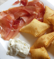 Crescentine, prosciutto crudo and squacquerone cheese creating delicious italian dish