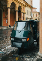 Charming three wheeled van, parked on a cobblestone street in bologna, italy, is glistening with raindrops after a recent rain shower