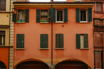 Italian charm in bologna, orange building with green shutters, arched porticos, potted plants, and open windows