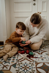 Grandmother and grandson in beige knitted sweaters look at vintage Christmas balls.