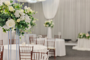 Decorated interior for festive event. Fancy table set for dinner with white flower composition in restaurant, luxury interior background. Wedding elegant banquet decoration arranged by catering